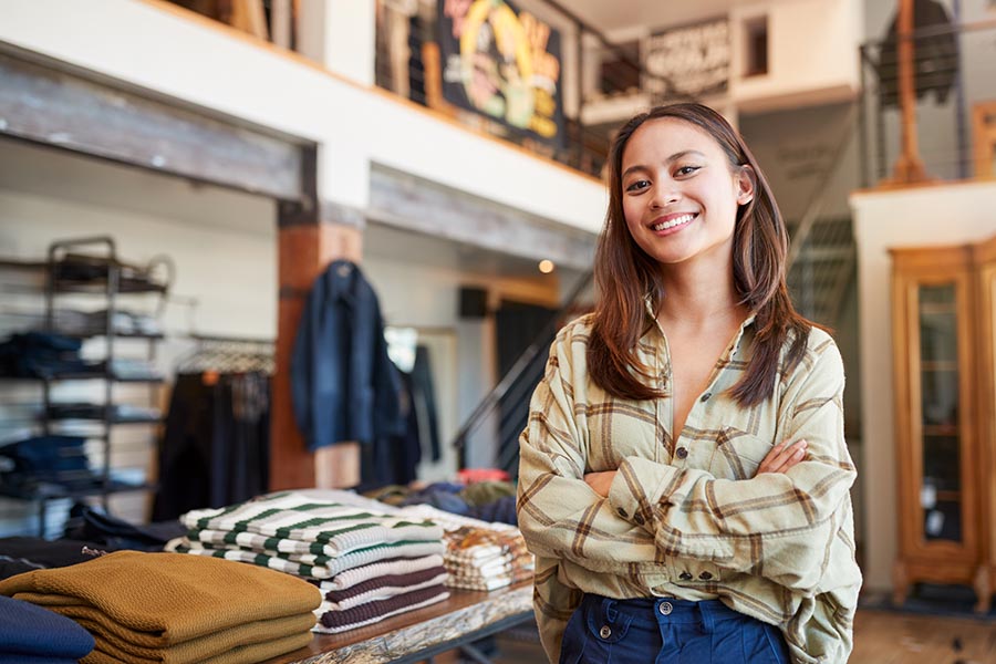 Business Insurance - Young Business Owner Smiles With Arms Crossed in Front of Her Clothing Store