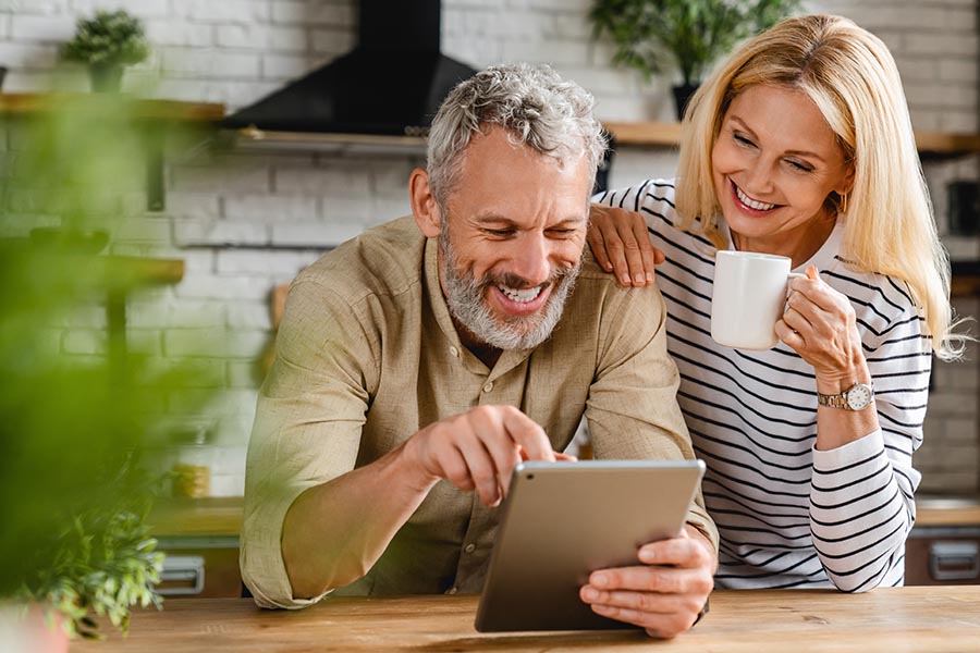 Contact Us - Couple Uses a Tablet at Their Kitchen Island While Enjoying Coffee, Smiling